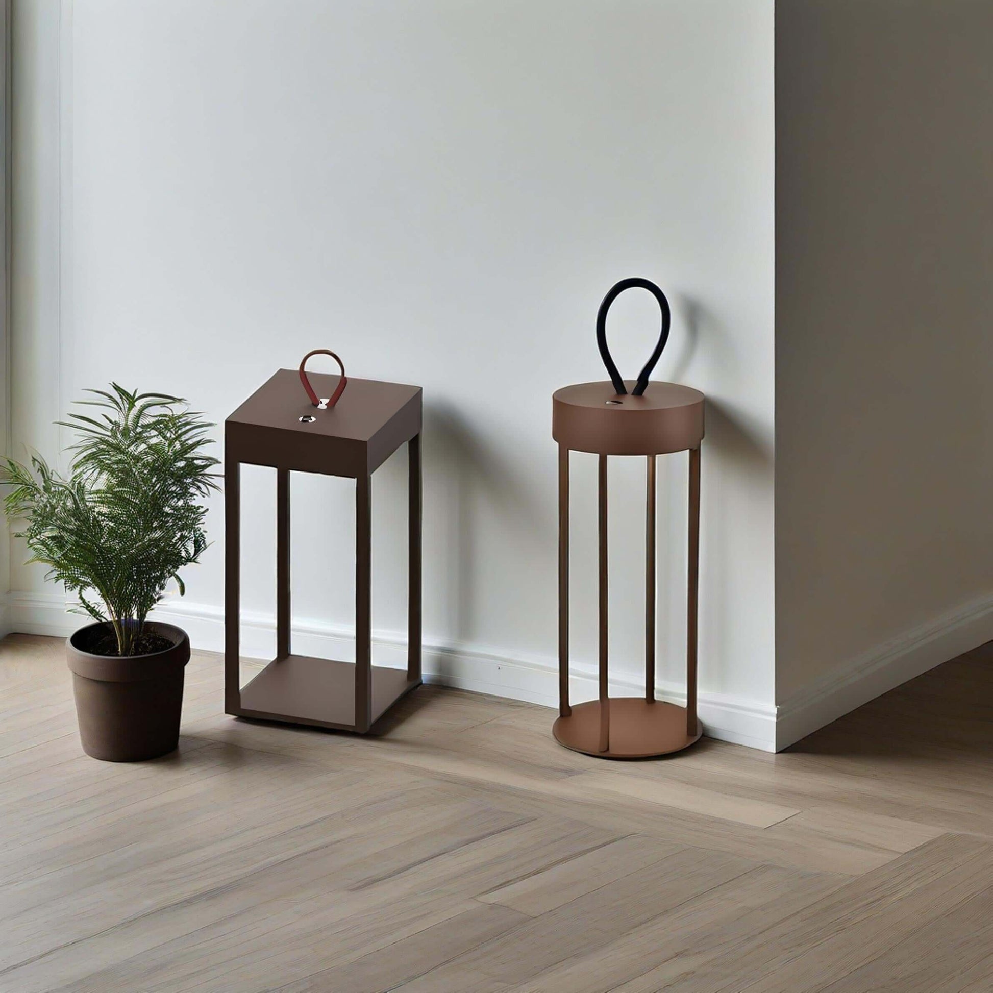 Two modern portable table lamps in brown, one with a handle, and a potted plant beside them.